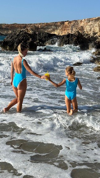 'Mini ARIEL' 3 Two women in blue swimsuits hold hands while standing in the ocean, enjoying a sunny day together.