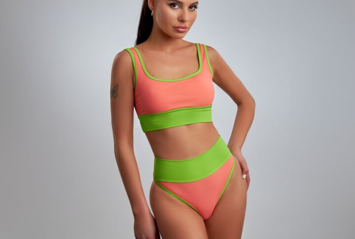 A woman wearing a green and orange bikini poses confidently on a beach